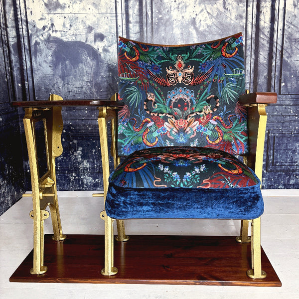 An original vintage cinema seat refurbished in Amazon Trip velvet by Mecca who.  Showing leopards wearing tiaras and snakes and boats it is heavily patterned.  The drop down seat has midnight blue velvet piping and panel.  The outside leg is a row end and features decorative details.  The cinema seat has a small wood table top attached at the side.