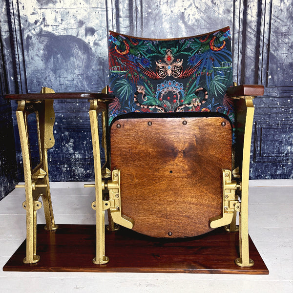An original vintage cinema seat refurbished in Amazon Trip velvet by Mecca who.  Showing leopards wearing tiaras and snakes and boats it is heavily patterned.  The drop down seat has midnight blue velvet piping and panel.  The outside leg is a row end and features decorative details.  The cinema seat has a small wood table top attached at the side.