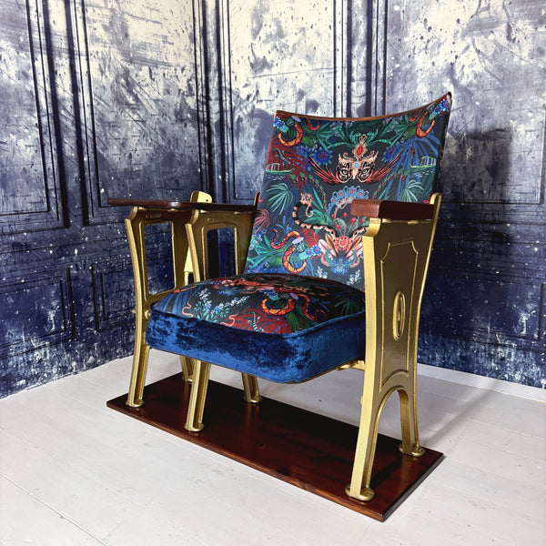 An original vintage cinema seat refurbished in Amazon Trip velvet by Mecca who.  Showing leopards wearing tiaras and snakes and boats it is heavily patterned.  The drop down seat has midnight blue velvet piping and panel.  The outside leg is a row end and features decorative details.  The cinema seat has a small wood table top attached at the side.