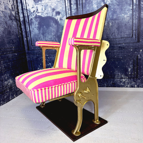 Vintage cinema seat with pink and yellow striped velvet from colours of arley, against a textured blue wall.