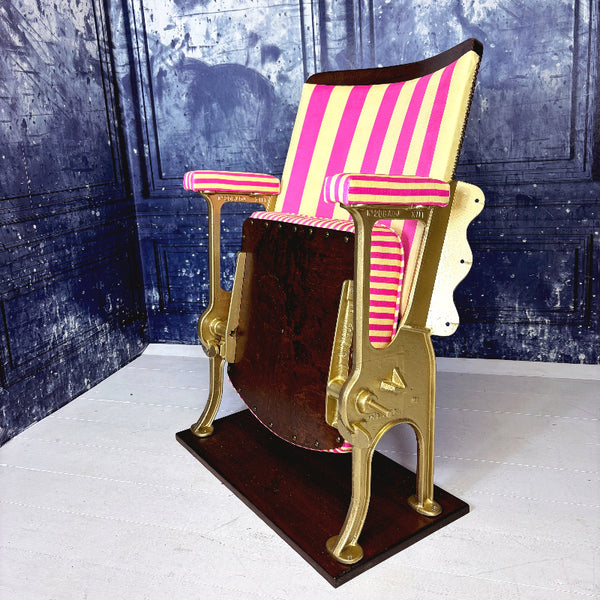 Vintage cinema seat with pink and yellow striped velvet from colours of arley, against a textured blue wall.