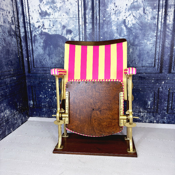 Vintage cinema seat with pink and yellow striped velvet from colours of arley, against a textured blue wall.