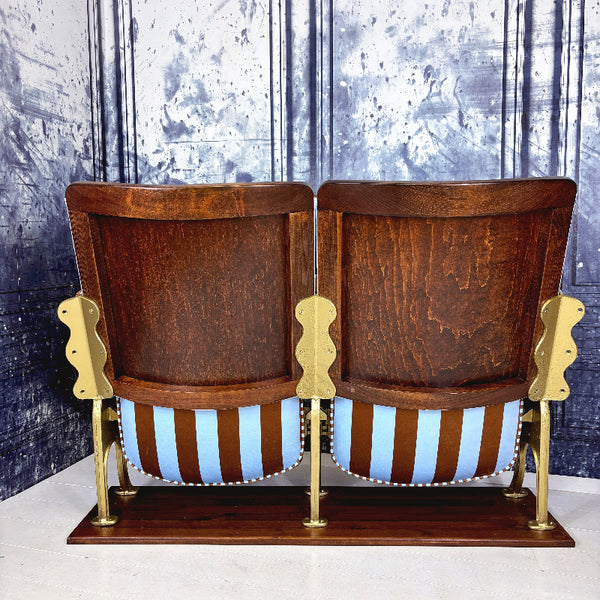 Pair of wooden theater seats with gold frames and blue  and brown striped upholstery against a textured wall.