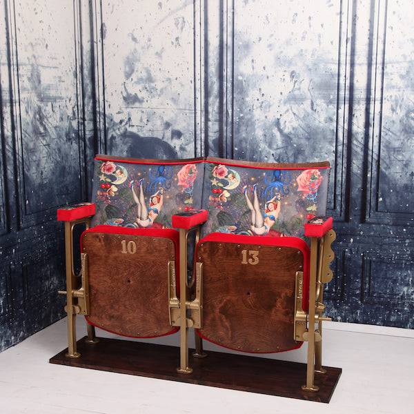 a set of two vintage cinema seat against a marbled blue wallpaper. Cinema seats are upholstered in Fifi velvet with red velvet piping and border