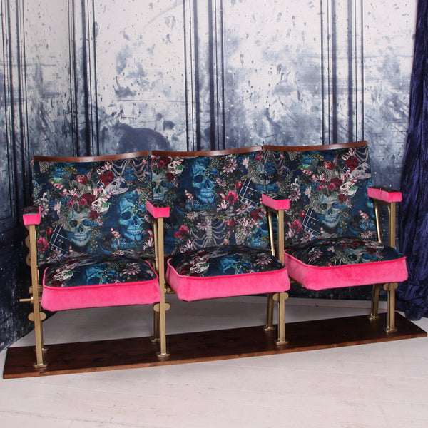 Set of three vintage cinema seats with seats down, upholstered in blue skull velvet with pink piping and panels.  The seats are in front of a blue marbled wall.