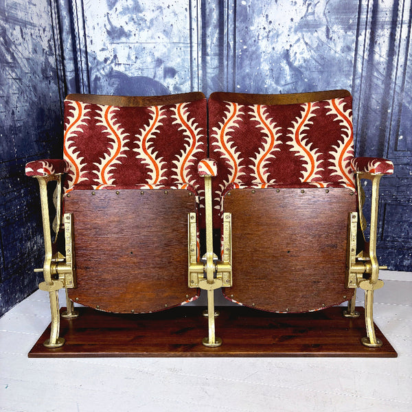Pair of vintage theater seats with patterned cushions against a textured wall.