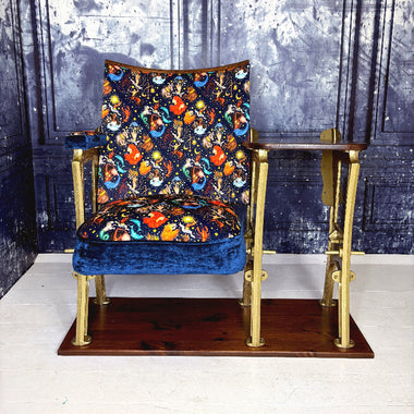 Vintage refurbished vintage cinema seat with colourful patterned velvet upholstery depicting the zodiac signs.  The sat is on a wooden base and positioned against a blue marbled wall.