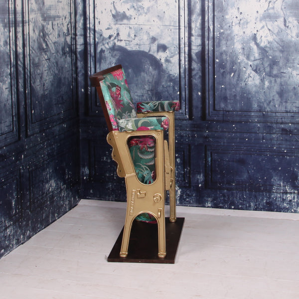 A SINGLE VINTAGE CINEMA SEAT UPHOLSTERED IN A PINK AND GREEN VELVET WITH ANIMALS AND AIR BALLOONS ON IT.  THE CHAIR IS IN FRONT OF A BLUE WALL