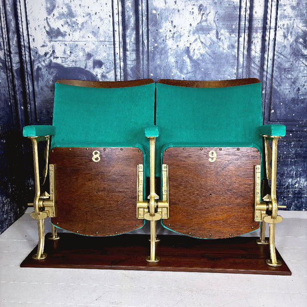 Pair of vintage theater seats with green backrests and gold metal frames against a textured wall.