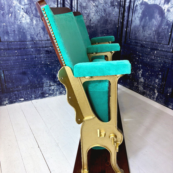 Jade green velvet theater seats with gold legs on a white floor against a blue wall.