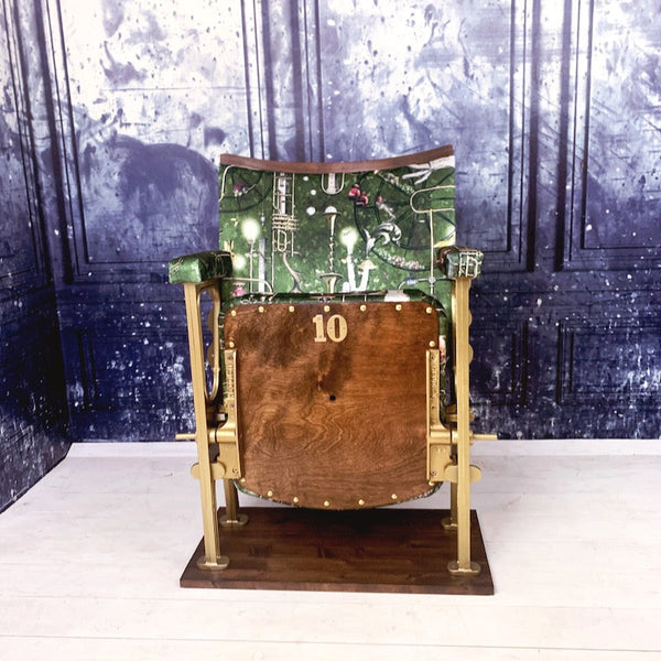 A single vintage cinema seat upholstered in a green velvet with mice and brass instruments on it.  The seat is closed showing the wood seat base.
