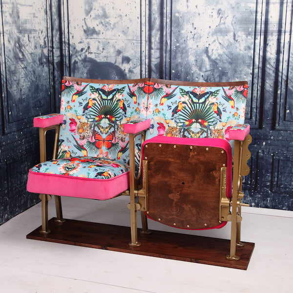 Set of two vintage cinema seats against a blue marbled wallpaper. Seats are upholstered in a flower and butterfly pattern blue velvet with pink piping and panelling