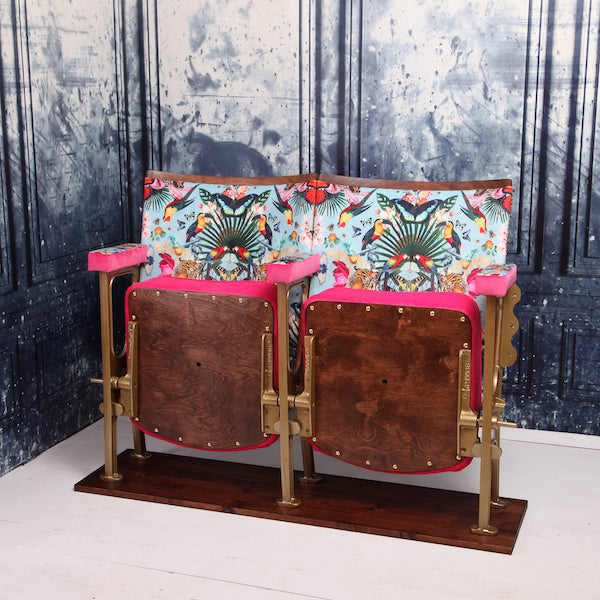 Set of two vintage cinema seats against a blue marbled wallpaper. Seats are upholstered in a flower and butterfly pattern blue velvet with pink piping and panelling