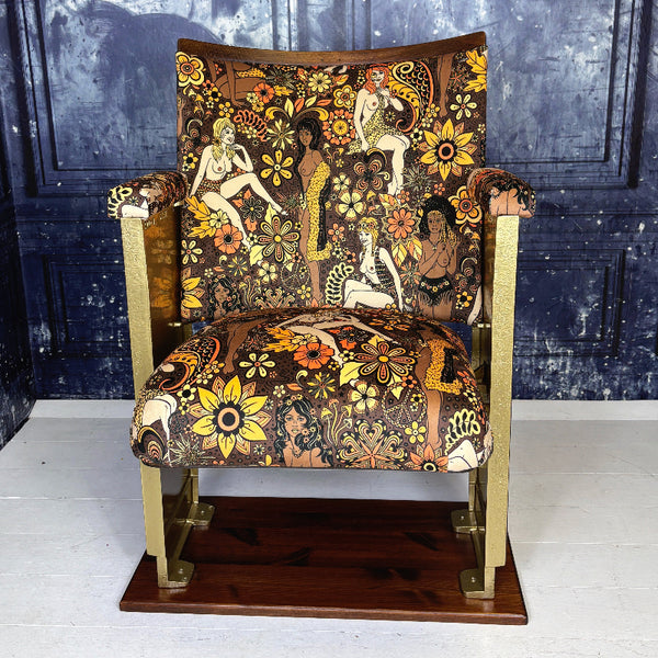 Decorative vintage cinema seat with intricate floral and figurative patterns against a dark blue wall.

